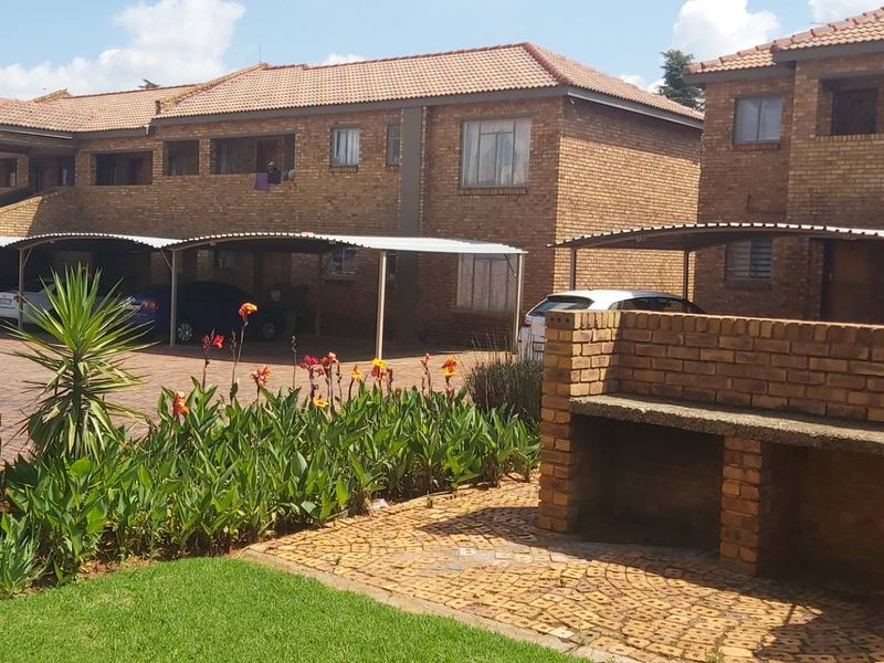 Exterior view of a face brick apartment complex featuring covered carports, a communal garden area, and a built-in brick braai facility.