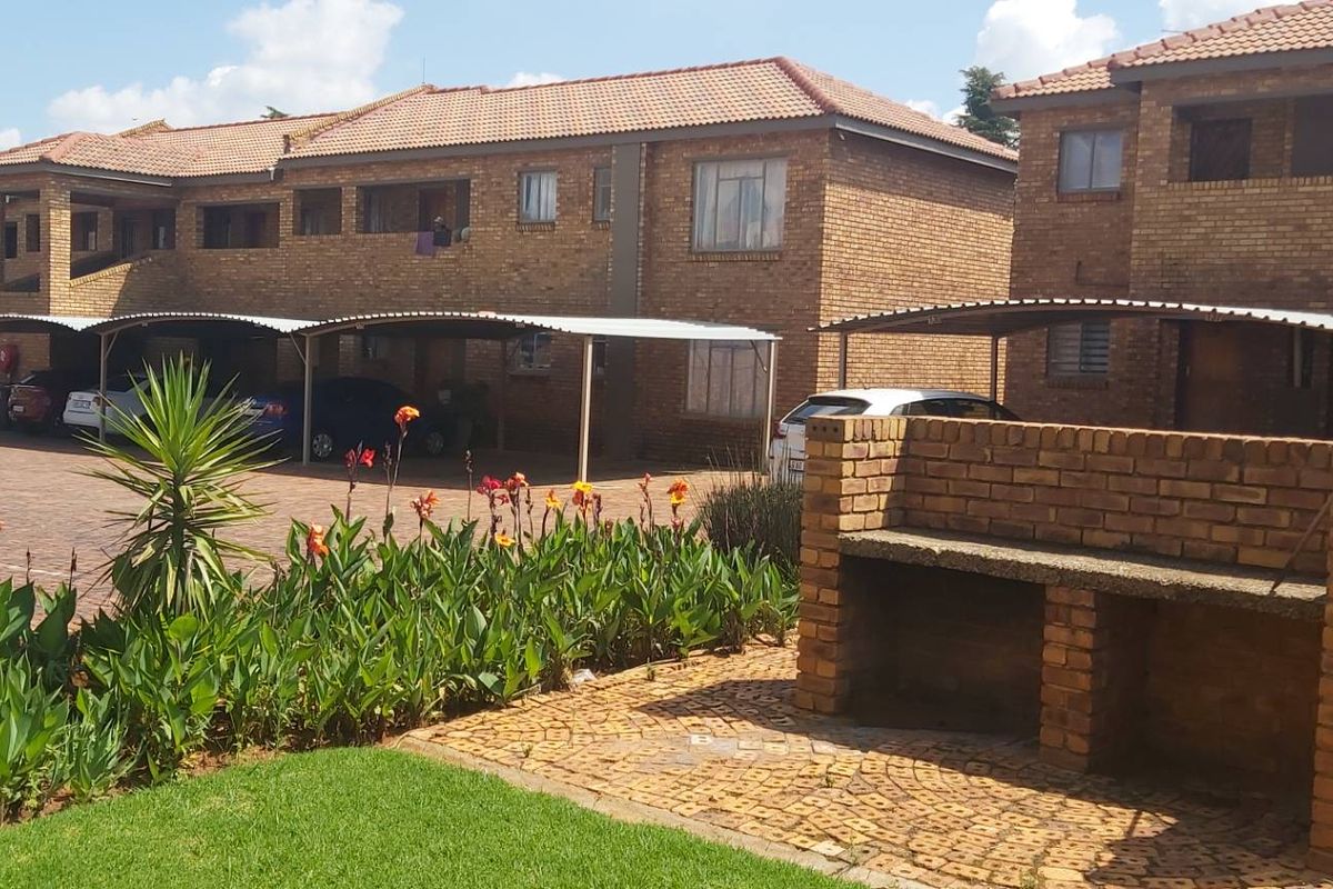 Exterior view of a face brick apartment complex featuring covered carports, a communal garden area, and a built-in brick braai facility.