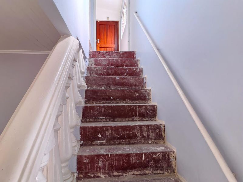 Interior staircase featuring a traditional balustrade and handrail, leading to an upper level with a timber door.