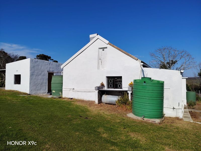 Rear view of a white-painted cottage featuring external water storage tanks, security bars on windows, and a grassed yard area.
