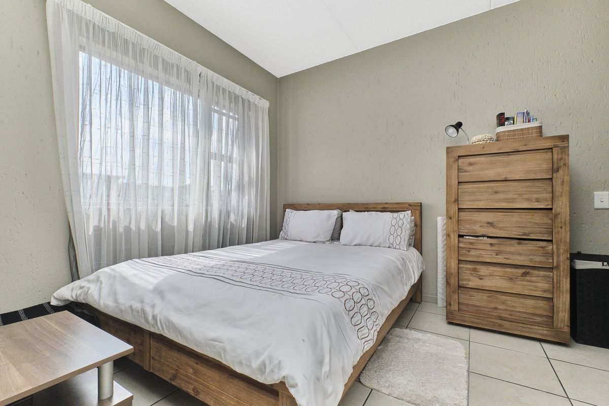 A functional bedroom featuring tiled flooring and neutral textured walls, offering a clean and simple living space.