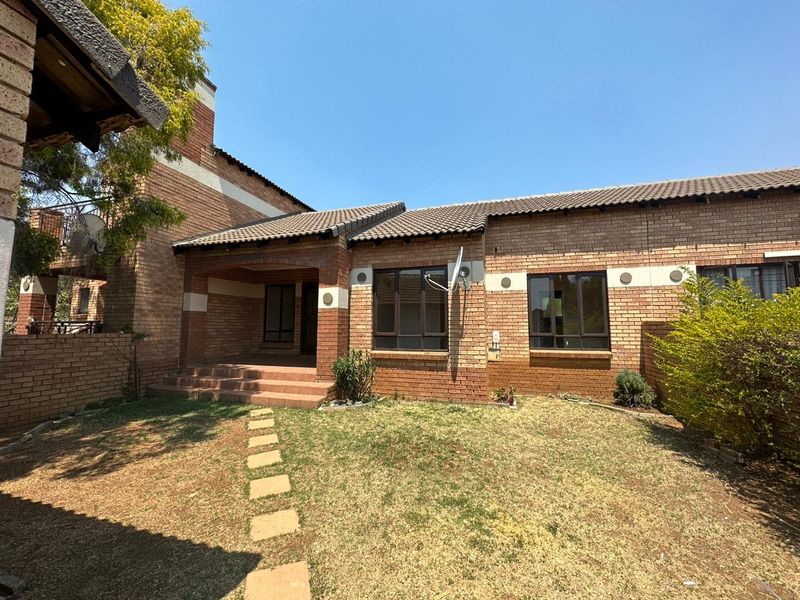 Front view of a face brick townhouse featuring a covered entrance porch, tiled roof, and a small front garden with a stone pathway.