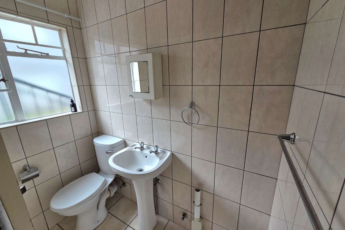 A functional bathroom featuring a pedestal sink, toilet, and full-height wall tiling, offering a clean and practical layout.
