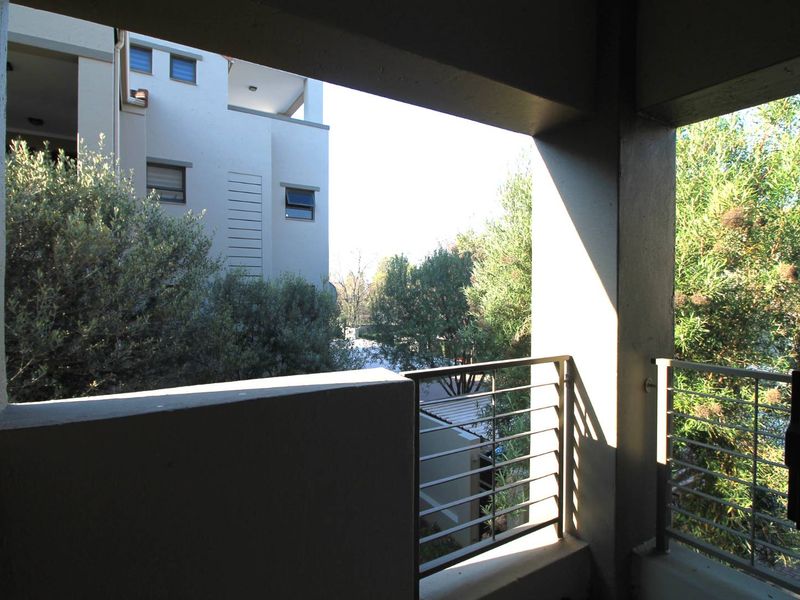 A covered balcony featuring a metal balustrade and concrete structure, offering an elevated view of the surrounding apartment complex and greenery.
