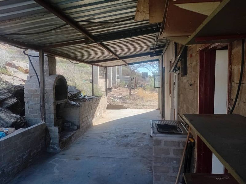 A covered outdoor patio area featuring a built-in brick braai, concrete flooring, and a corrugated metal roof, offering potential for an outdoor entertainment space.