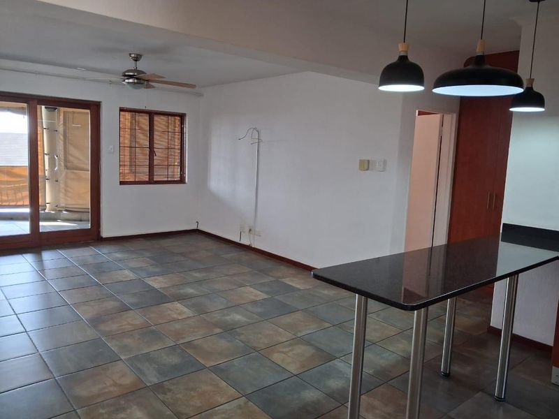 Spacious open-plan living area featuring tiled floors, a breakfast bar, modern pendant lighting, and direct access to a balcony through sliding glass doors.