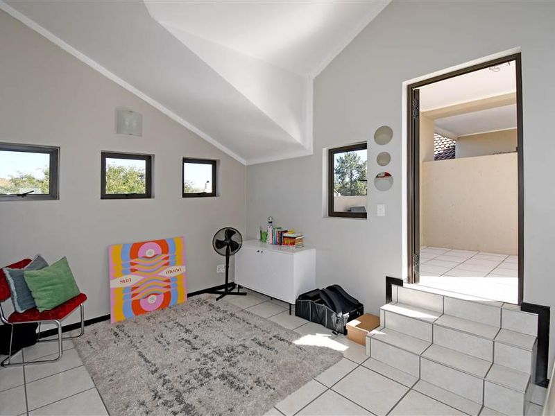 A bright living area featuring vaulted ceilings, tiled flooring, and direct access to an outdoor patio area via a small set of tiled steps.