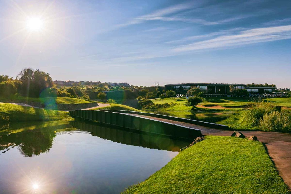 A scenic view of a well-maintained golf course featuring a pedestrian bridge over a water feature and lush landscaped surroundings.