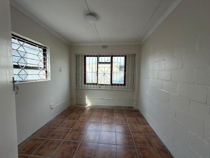 An empty bedroom featuring tiled flooring, security bars on windows, and an exposed brick wall, offering a blank canvas for renovation.