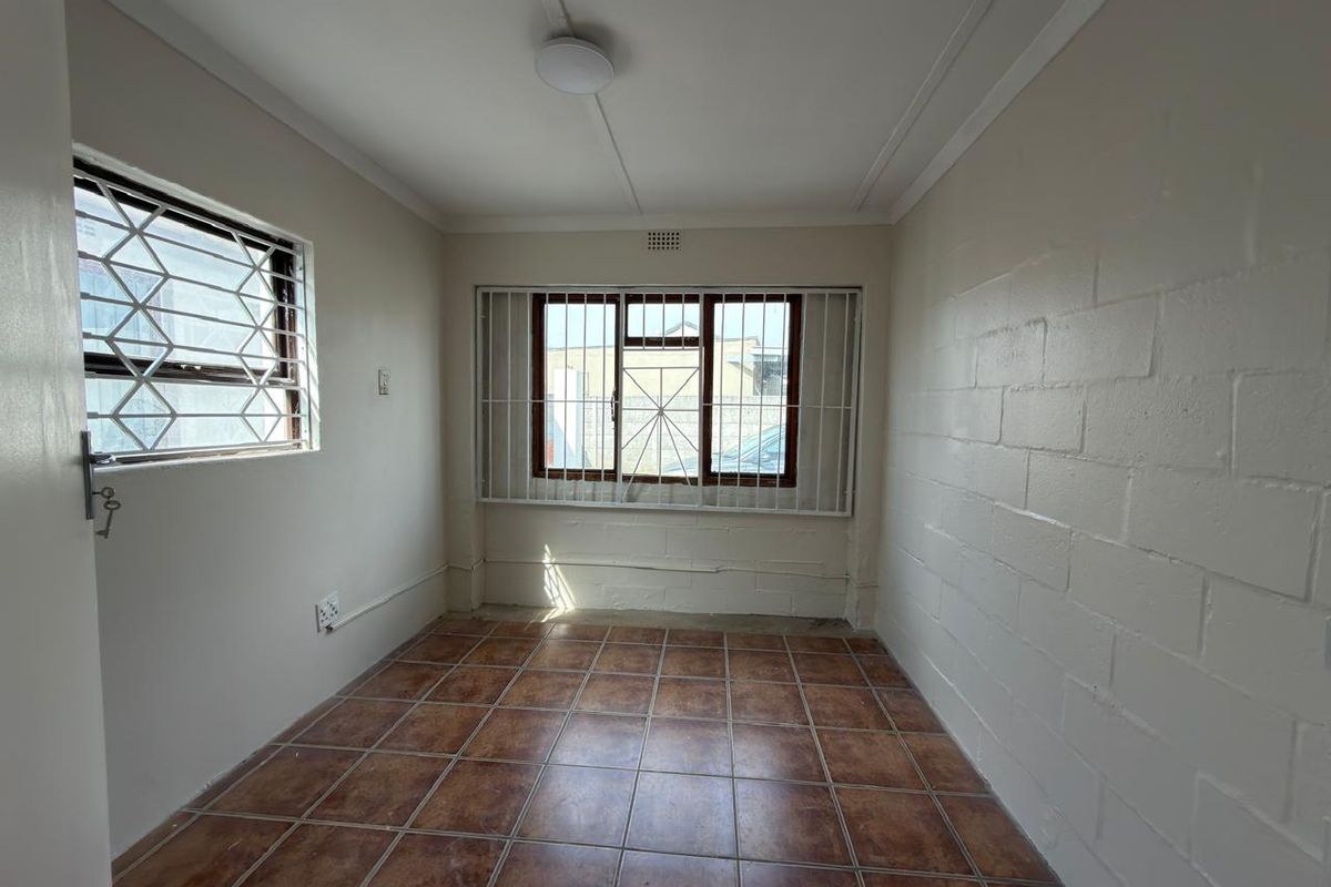 An empty bedroom featuring tiled flooring, security bars on windows, and an exposed brick wall, offering a blank canvas for renovation.