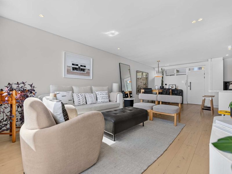 A bright and modern open-plan living and kitchen area featuring light timber flooring and recessed downlighting throughout.