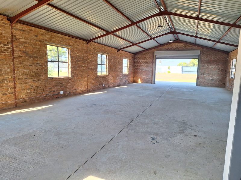 Spacious industrial utility area featuring exposed brick walls, concrete flooring, and high-clearance steel roof trusses with a large roller shutter door.