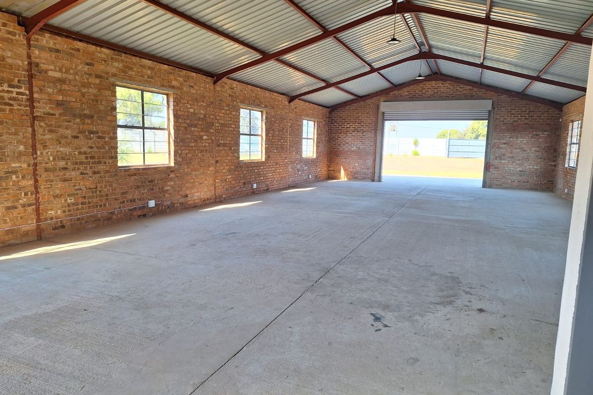 Spacious industrial utility area featuring exposed brick walls, concrete flooring, and high-clearance steel roof trusses with a large roller shutter door.