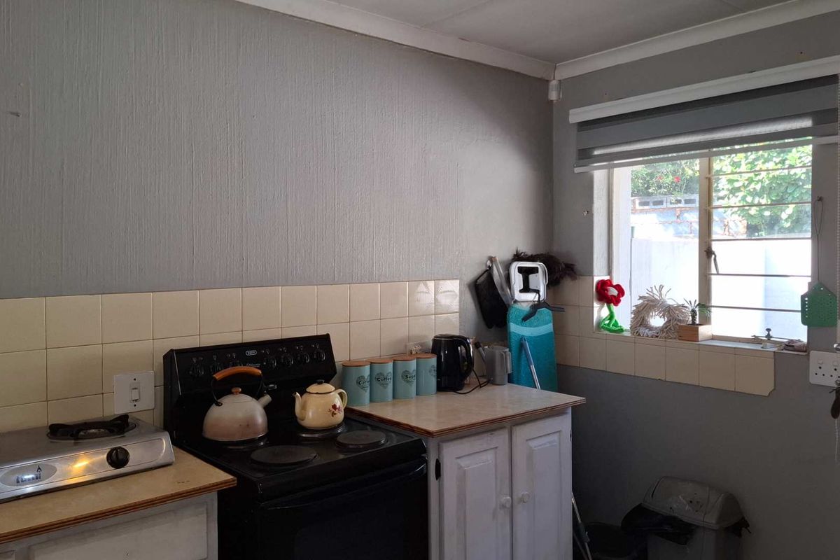 A compact kitchen area featuring a freestanding stove, tiled splashback, and built-in cabinetry, offering potential for modernization and improved layout efficiency.