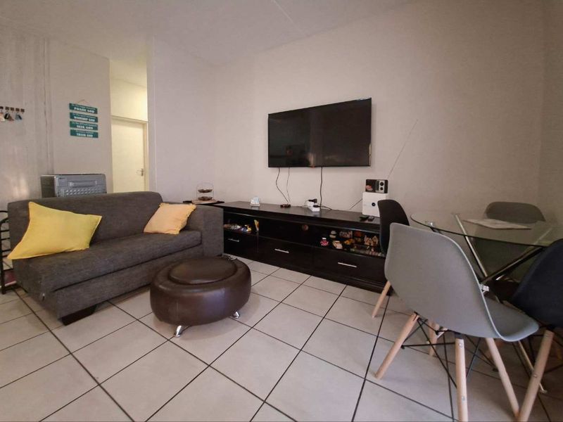 Open plan living and dining area featuring neutral ceramic floor tiles and a wall-mounted television.