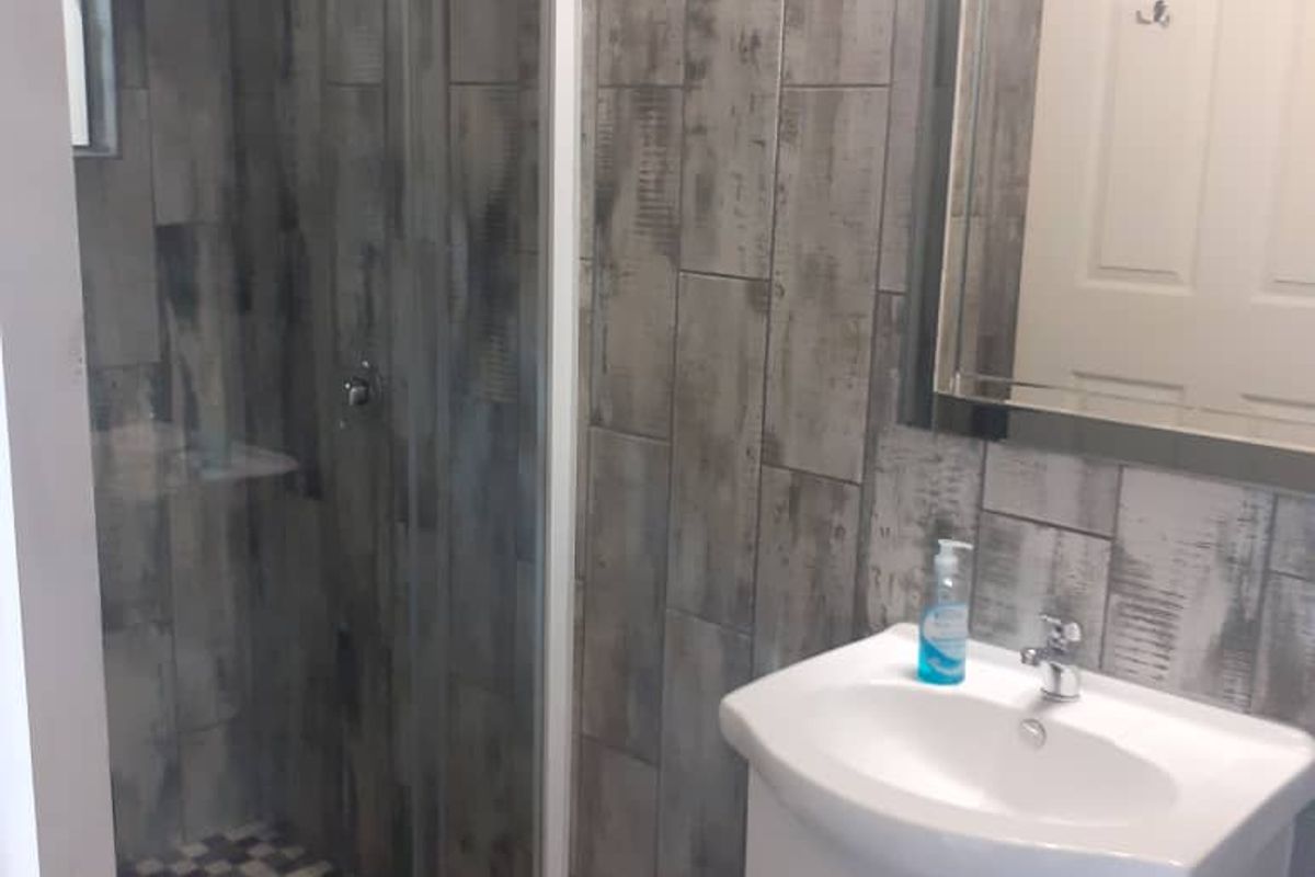 A modern bathroom featuring a glass-enclosed shower with patterned floor tiles, a vanity basin, and rustic-style wall tiling.