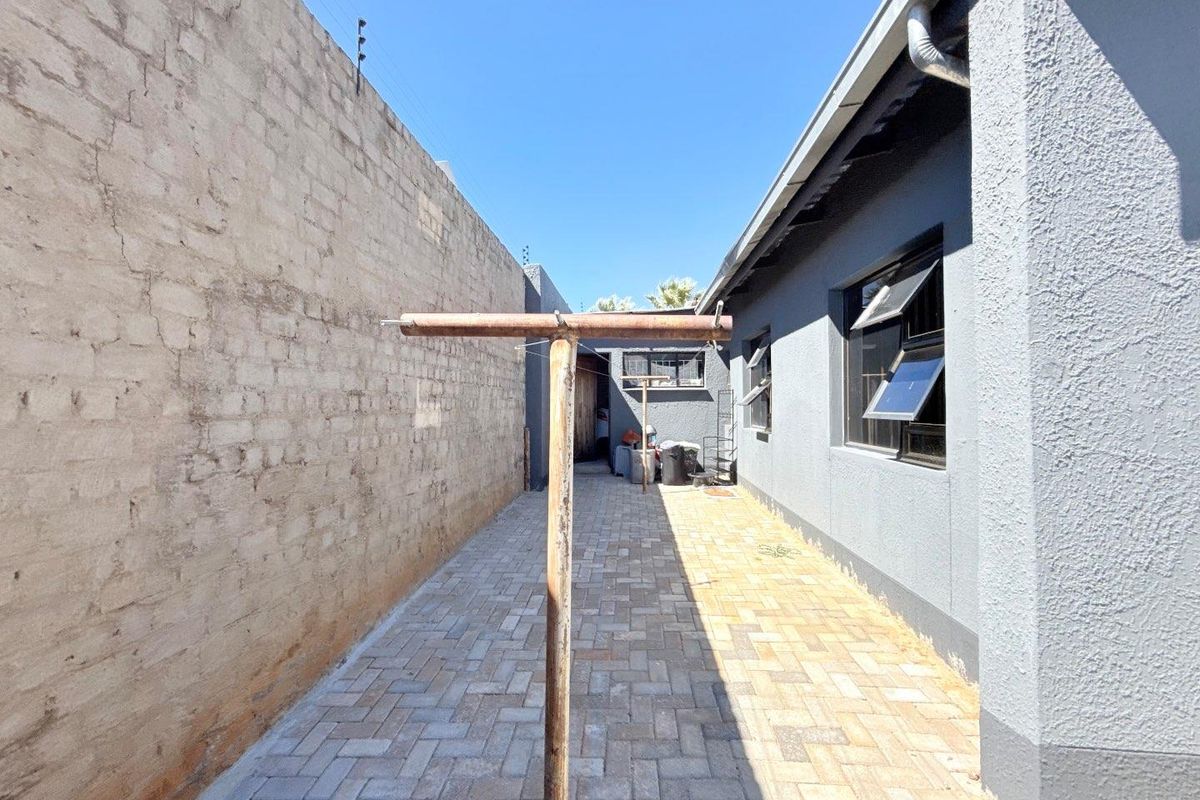 Side exterior area featuring paved flooring, a boundary wall with electric fencing, and a fixed metal washing line.