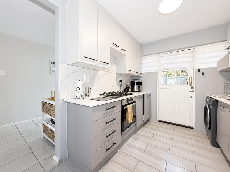 Modern kitchen featuring grey and white cabinetry, stone countertops, marble-look splashback, built-in oven, gas hob, and direct access to the exterior via a stable door.