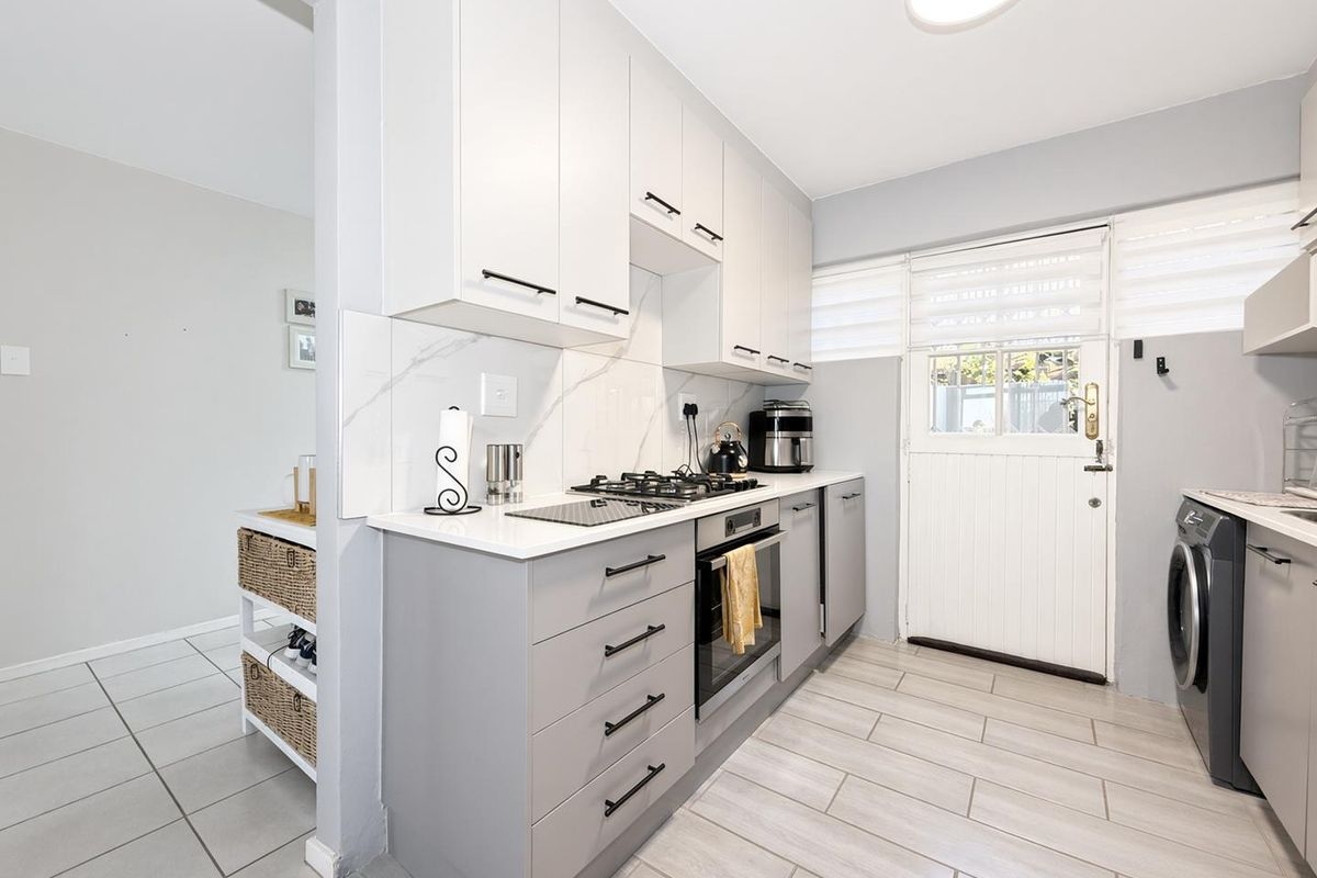 Modern kitchen featuring grey and white cabinetry, stone countertops, marble-look splashback, built-in oven, gas hob, and direct access to the exterior via a stable door.