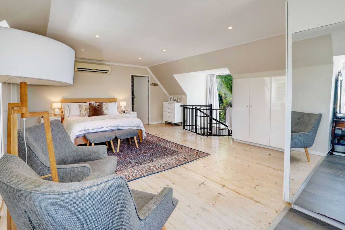 Spacious bedroom featuring light timber flooring, built-in cabinetry, recessed lighting, and an integrated air conditioning unit, with an open staircase leading to the lower level.