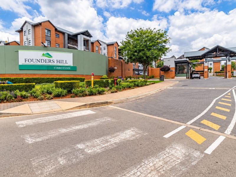 The entrance to Founders Hill Curro Estate, featuring a secure gatehouse, paved driveway, and well-maintained brick apartment buildings.