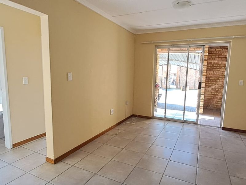 An empty, tiled living area featuring a sliding glass door leading to an outdoor patio, with an adjacent view into a bathroom.