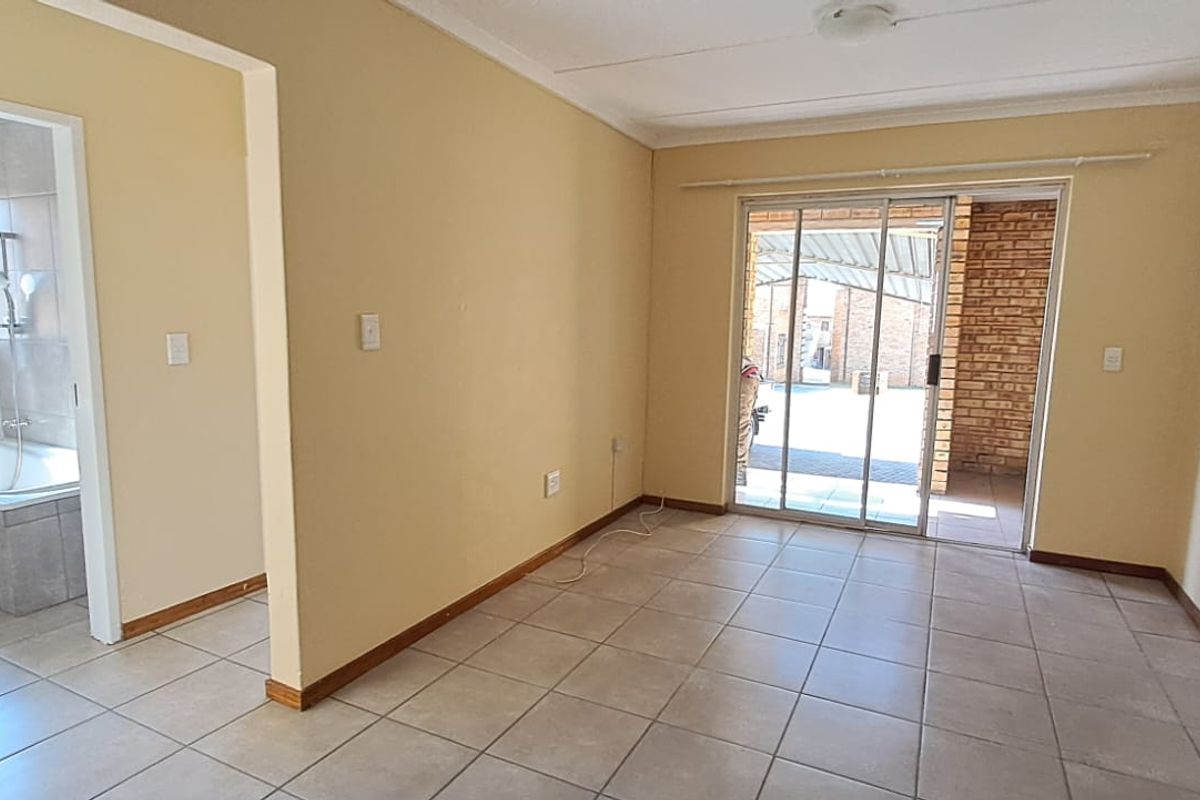 An empty, tiled living area featuring a sliding glass door leading to an outdoor patio, with an adjacent view into a bathroom.