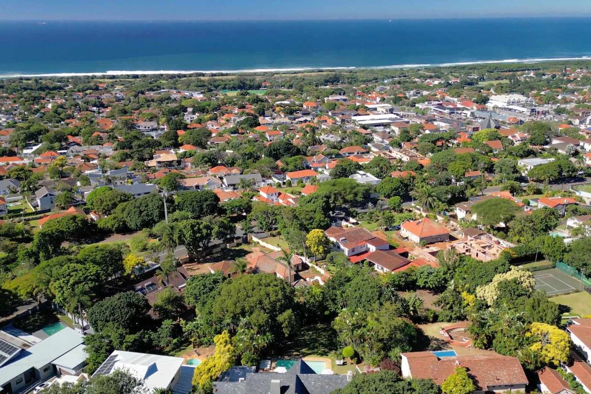 An elevated aerial view of a lush, green residential coastal neighborhood featuring numerous homes with tiled roofs and proximity to the ocean.