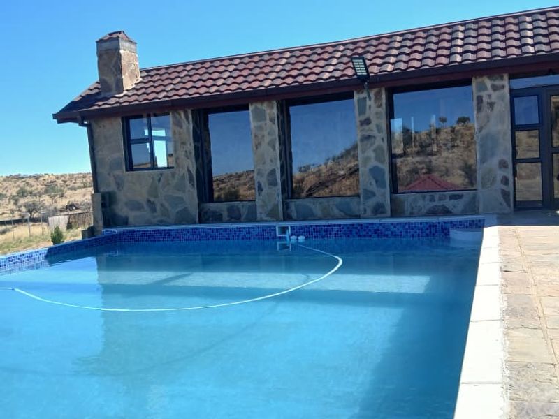 A well-maintained swimming pool area featuring stone-clad exterior walls, a tiled roof, and a paved deck, set against a scenic landscape.