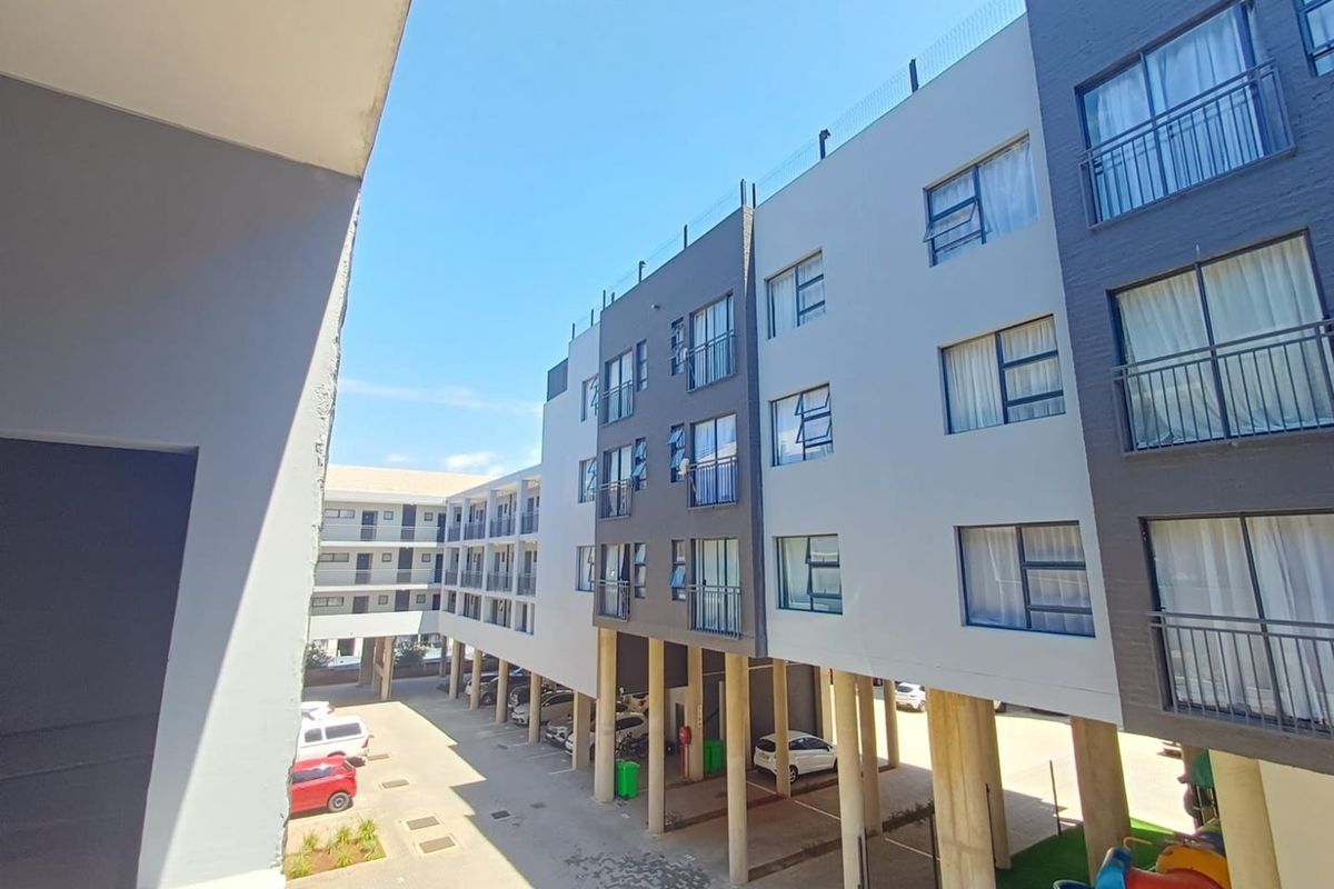 Exterior view of a modern apartment complex featuring elevated building structures, covered parking areas, and balconies with metal railings.