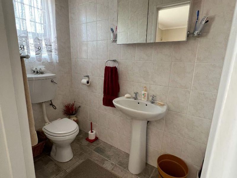 A functional guest bathroom featuring a pedestal basin, toilet, and wall-mounted medicine cabinet with neutral wall and floor tiling.