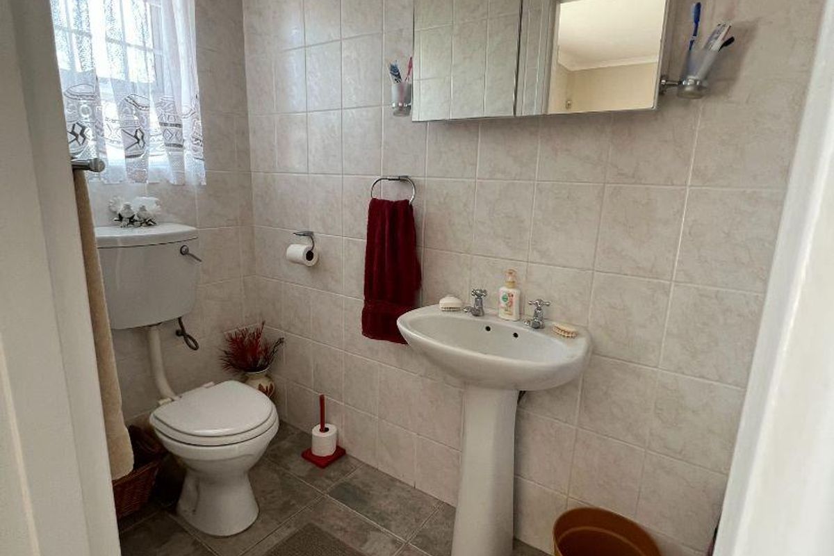 A functional guest bathroom featuring a pedestal basin, toilet, and wall-mounted medicine cabinet with neutral wall and floor tiling.