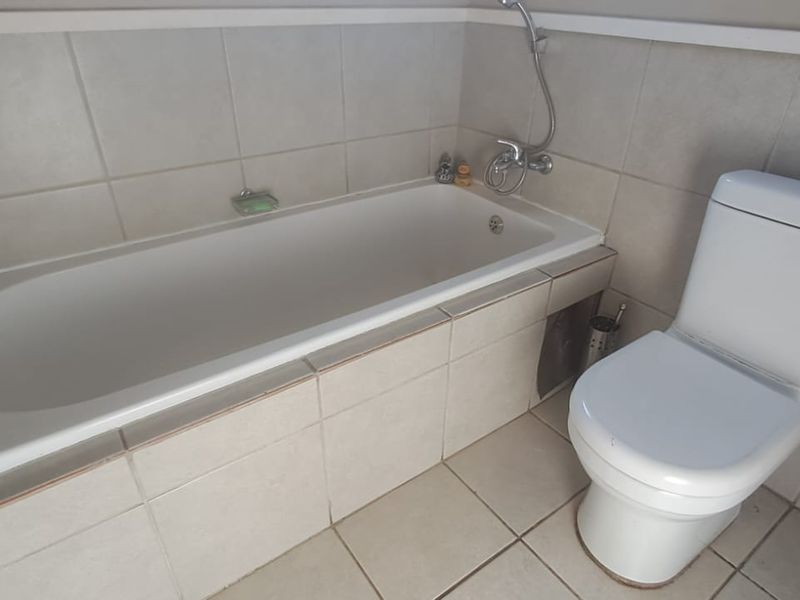 A functional bathroom featuring a built-in bathtub with shower mixer and a standard toilet, finished with neutral wall and floor tiling.