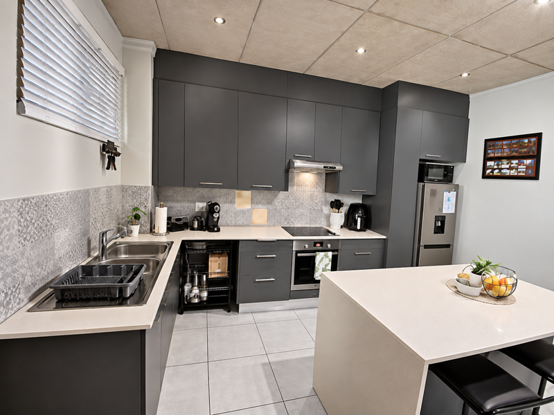 Modern kitchen featuring charcoal cabinetry, stone countertops, patterned tile backsplash, integrated appliances, and a central island with breakfast bar seating.