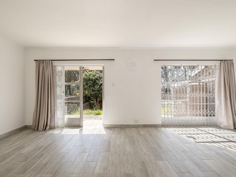 Bright and spacious living area featuring modern wood-look tile flooring, security gates, and direct access to the outdoor garden area.