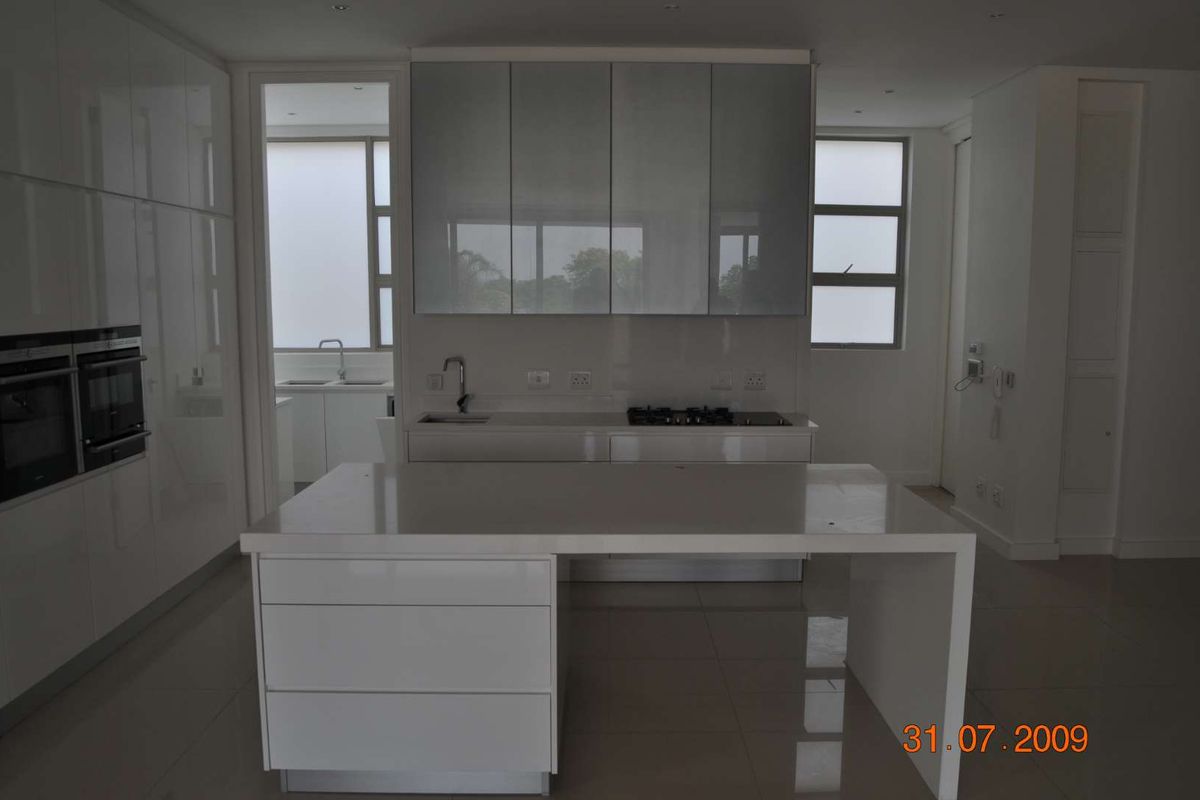 Modern kitchen featuring high-gloss white cabinetry, a central island, built-in double ovens, and a gas hob, with an adjacent scullery area.