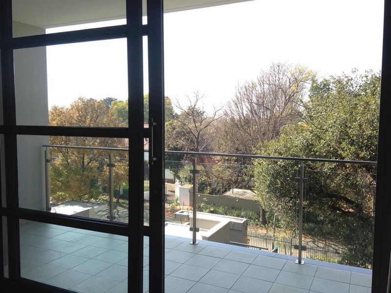 A clean, modern balcony featuring tiled flooring and a sleek glass balustrade, offering a pleasant view of the surrounding trees and neighborhood.
