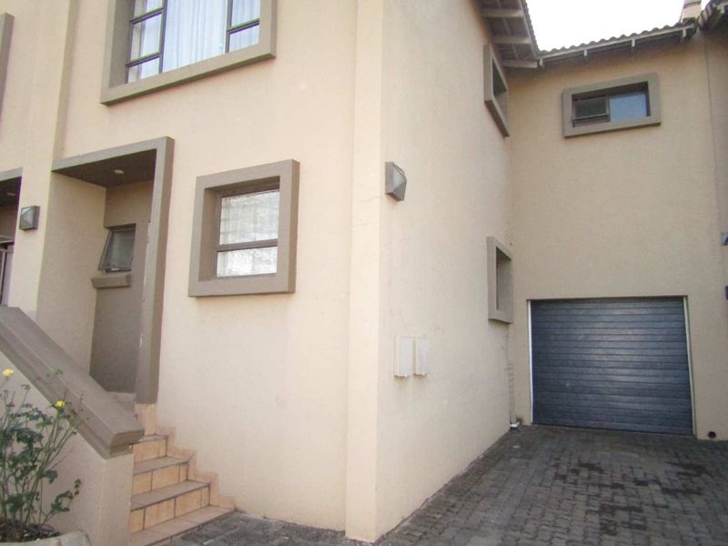 Front elevation of a townhouse featuring a paved driveway, single garage, and an external staircase leading to the entrance.