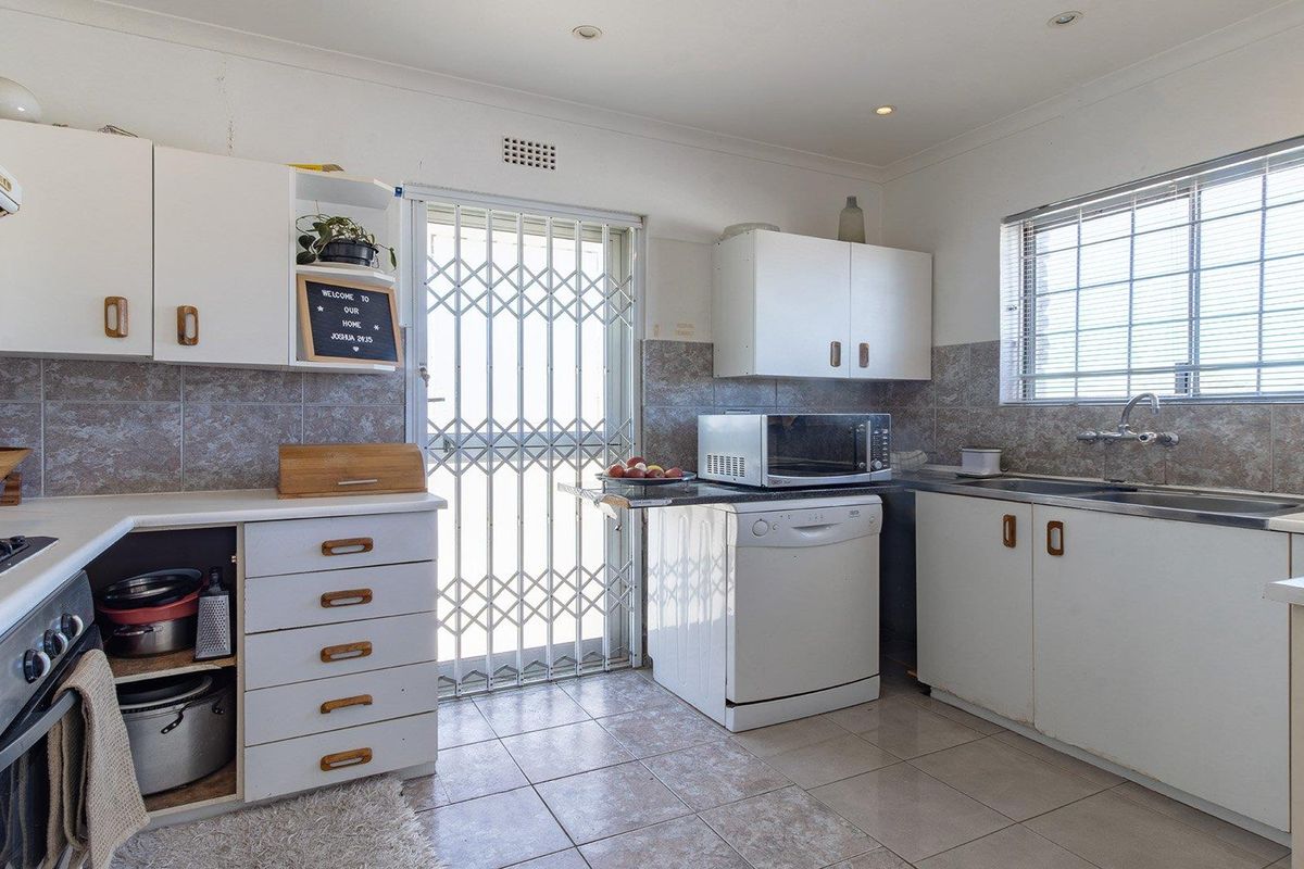 A functional kitchen featuring built-in cabinetry, tiled backsplash, integrated oven and hob, and a security gate leading to the exterior.