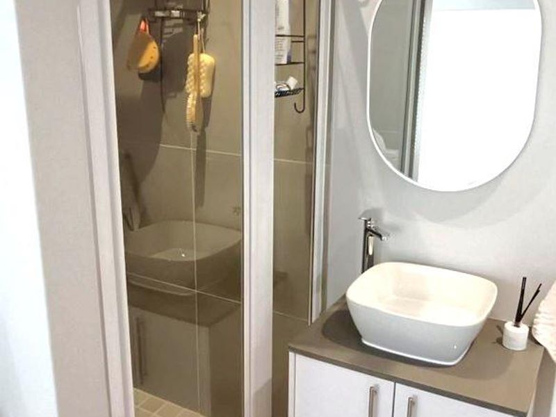 Modern bathroom featuring a wall-mounted vanity with a vessel sink, a sleek mixer tap, a circular mirror, and a glass-enclosed shower.