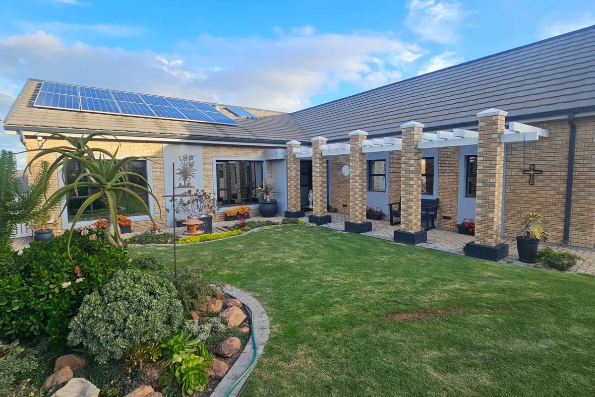 A well-maintained rear exterior featuring a brick facade, a covered pergola patio, landscaped garden, and roof-mounted solar panels.
