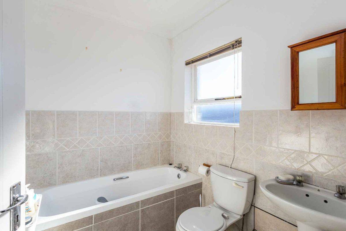 A functional bathroom featuring a bathtub, pedestal basin, and toilet with neutral wall tiling and a window for natural light.