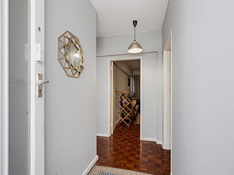 A clean, neutral-toned hallway featuring classic parquet flooring and a central pendant light fixture, providing access to adjacent rooms.