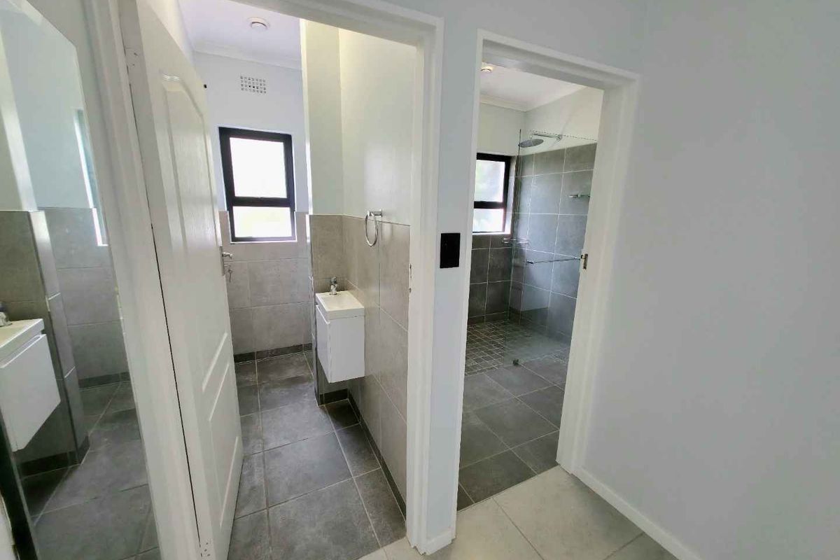 A modern bathroom featuring a walk-in shower with grey tiling, a wall-mounted vanity, and a separate toilet area with neutral finishes.