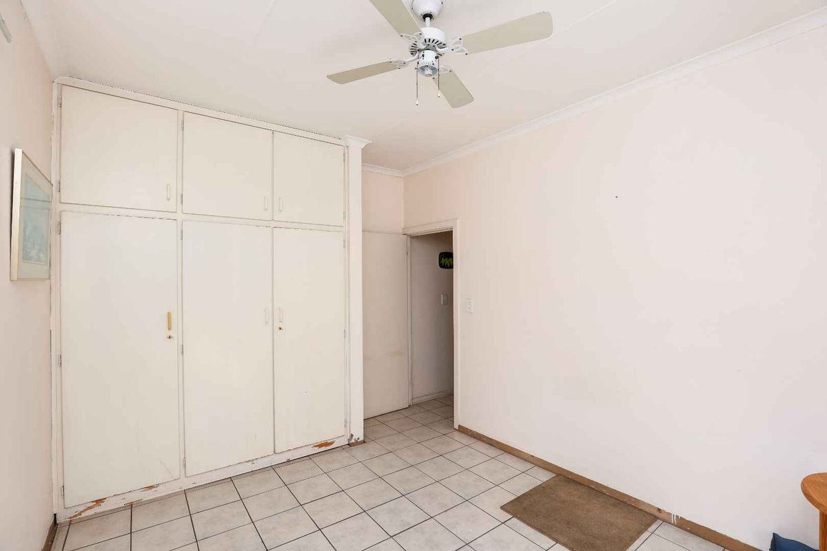 A bedroom featuring built-in cupboards, tiled flooring, and a ceiling fan, presenting a blank canvas for potential updates.
