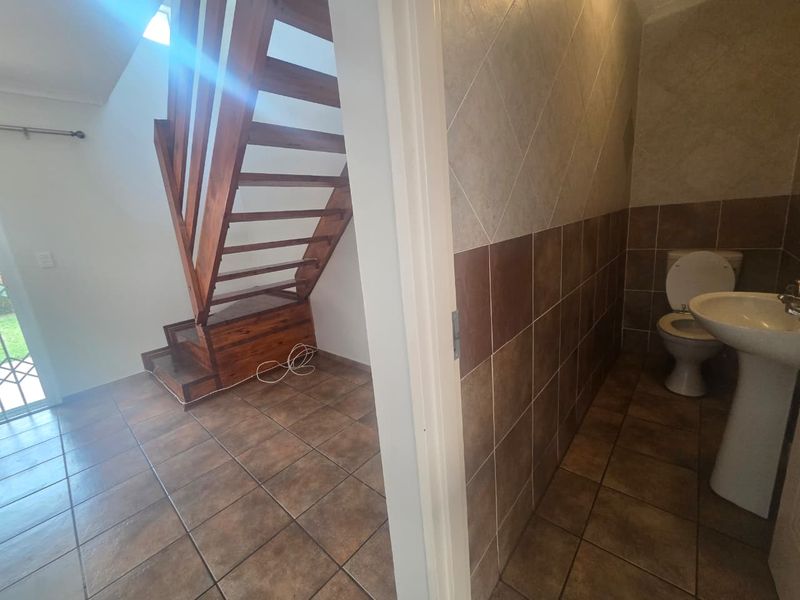 A view of a hallway featuring a wooden staircase and an adjacent bathroom with a pedestal basin and toilet.