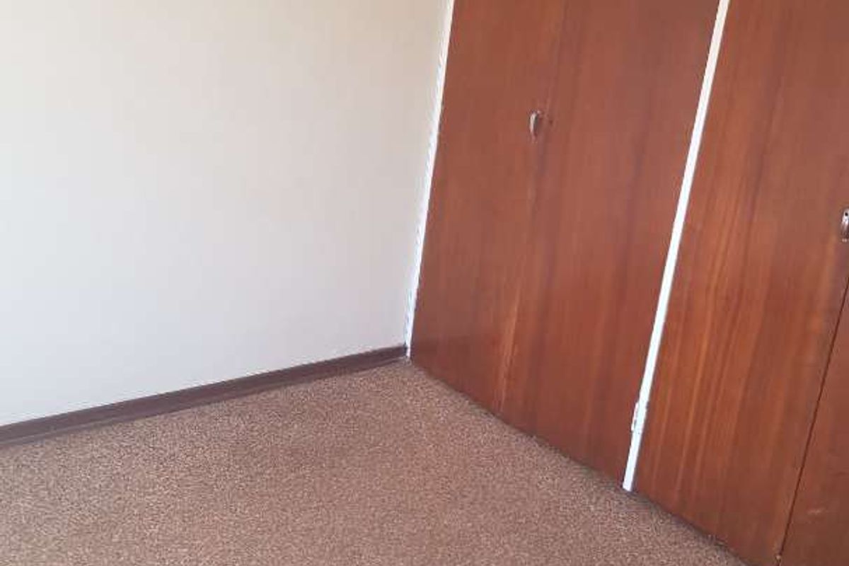 A vacant bedroom featuring built-in wooden cupboards and carpeted flooring, offering a blank canvas for potential updates and interior design.