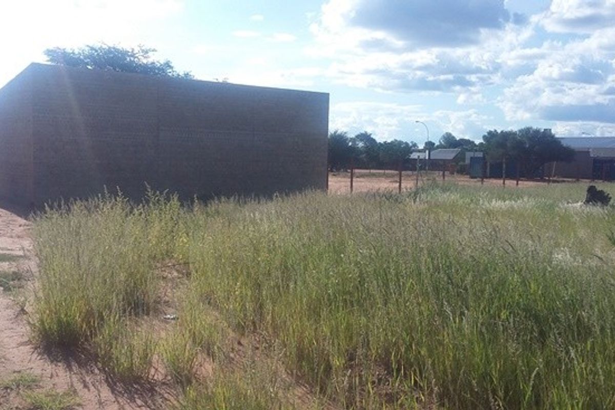 An exterior view of a vacant plot featuring a masonry wall and perimeter fencing, surrounded by overgrown grass and natural landscape.