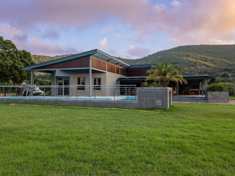 A modern residential property featuring a swimming pool, expansive lawn, and a covered patio area set against a scenic mountain backdrop.