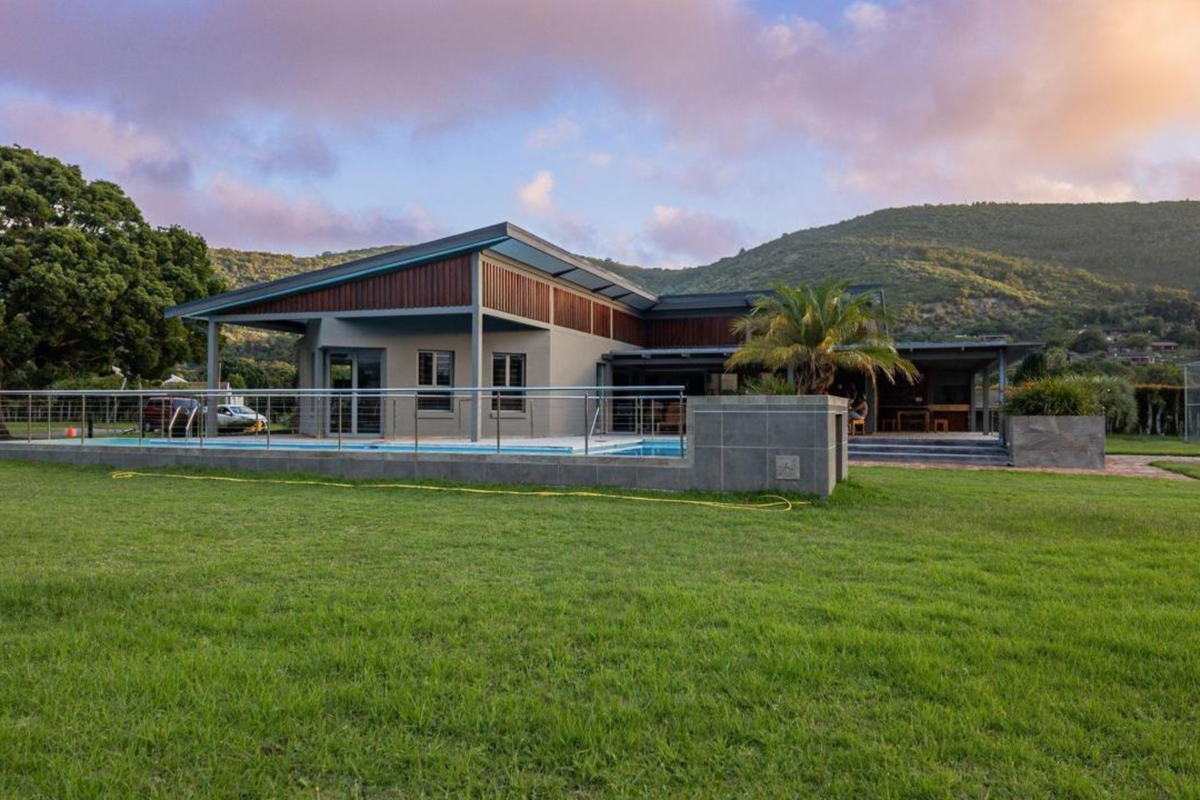 A modern residential property featuring a swimming pool, expansive lawn, and a covered patio area set against a scenic mountain backdrop.